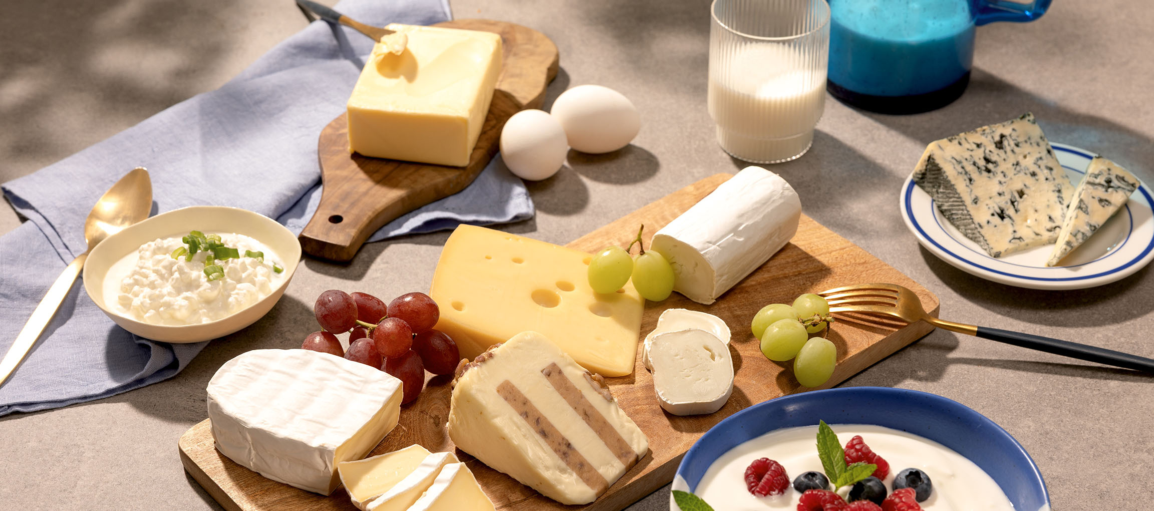 Válogatott sajtok, tojások, szőlő, tej és joghurt bogyós gyümölcsökkel egy asztalon.