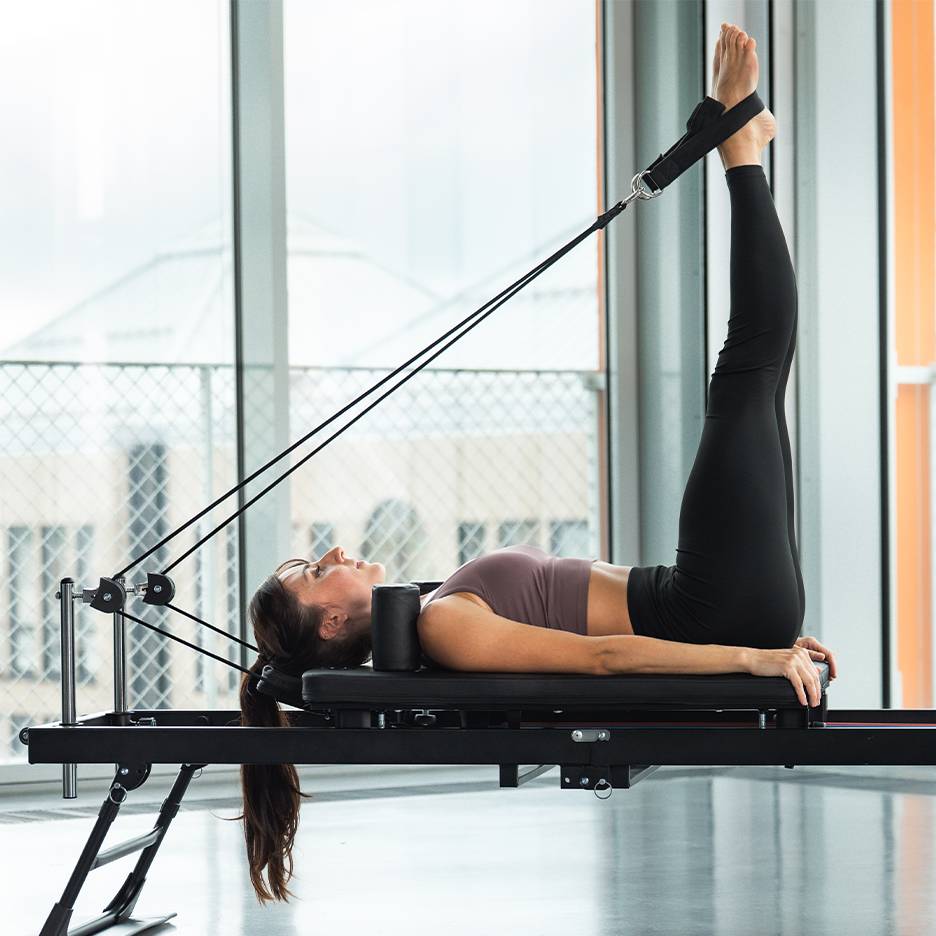 Nő lábgyakorlatot végez pilates reformer gépen.