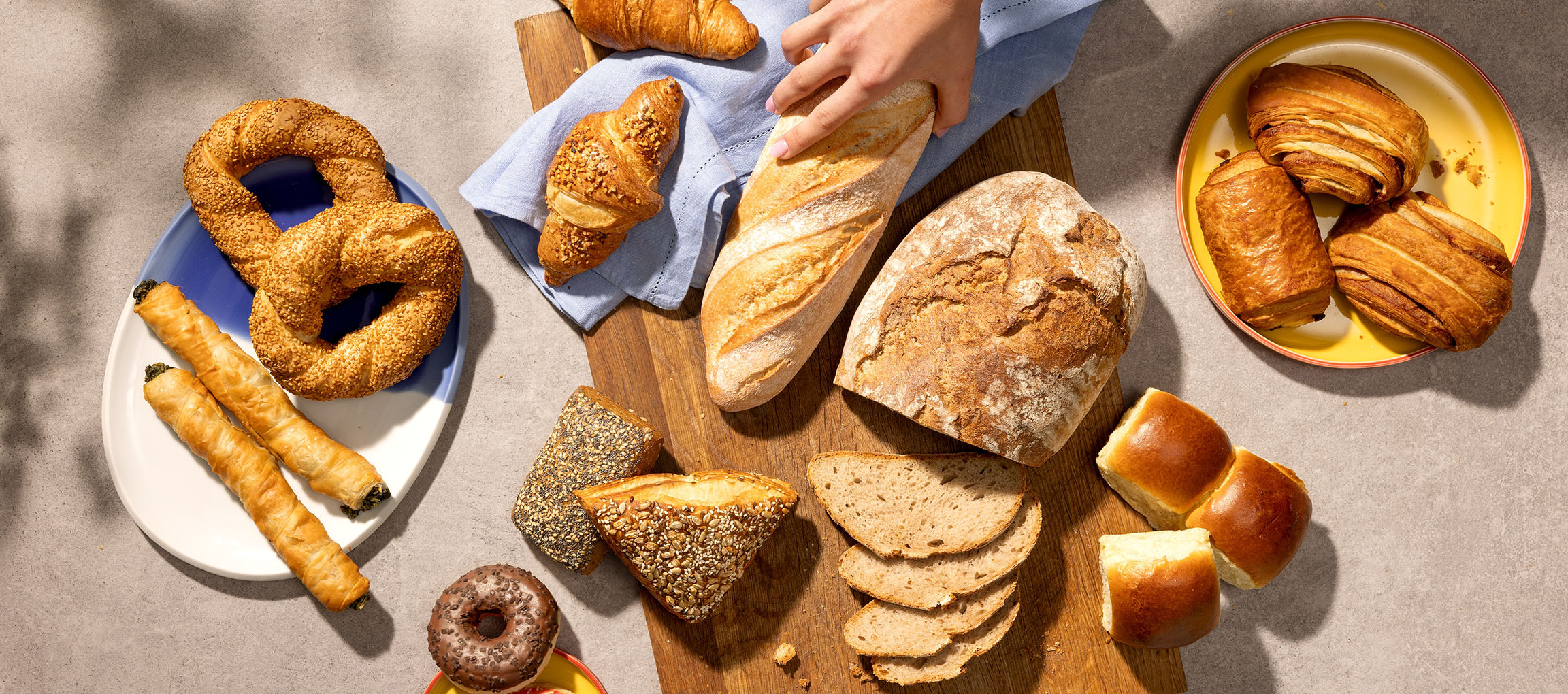 Különféle péksütemények és kenyerek, beleértve pereceket, croissant-okat és bagetteket, egy asztalon.