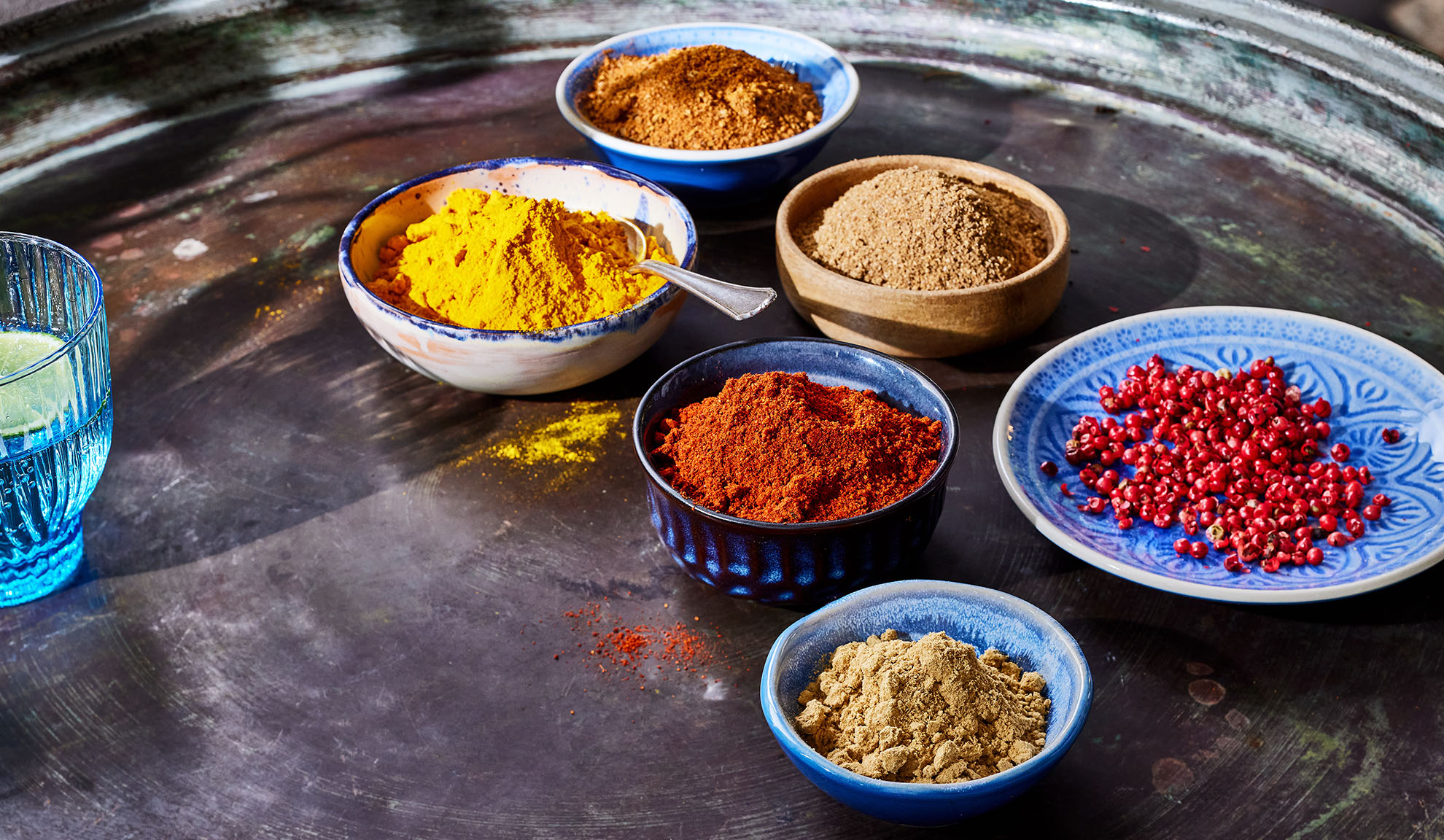 Különféle fűszerek tálkákban: kurkuma, paprika, bors és mások egy fém tálcán.