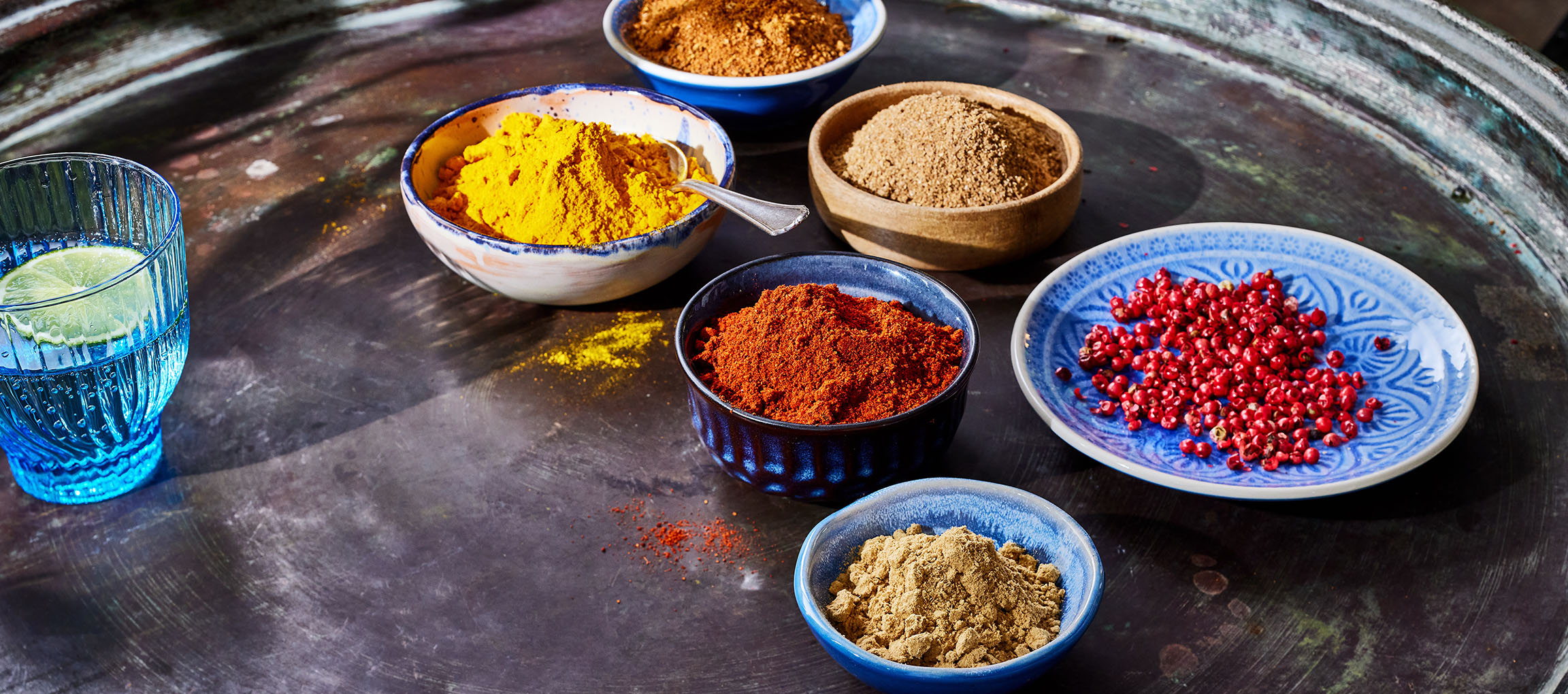 Különböző fűszerek, mint kurkuma, paprika és rózsabors, tálakban sötét alapon.