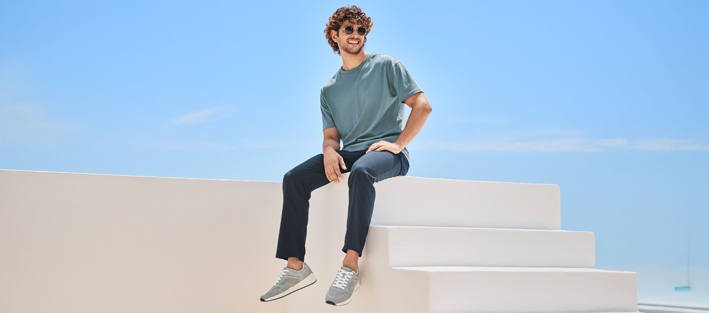 Férfi pólóban, nadrágban és New Balance cipőben, fehér lépcsőn ül.