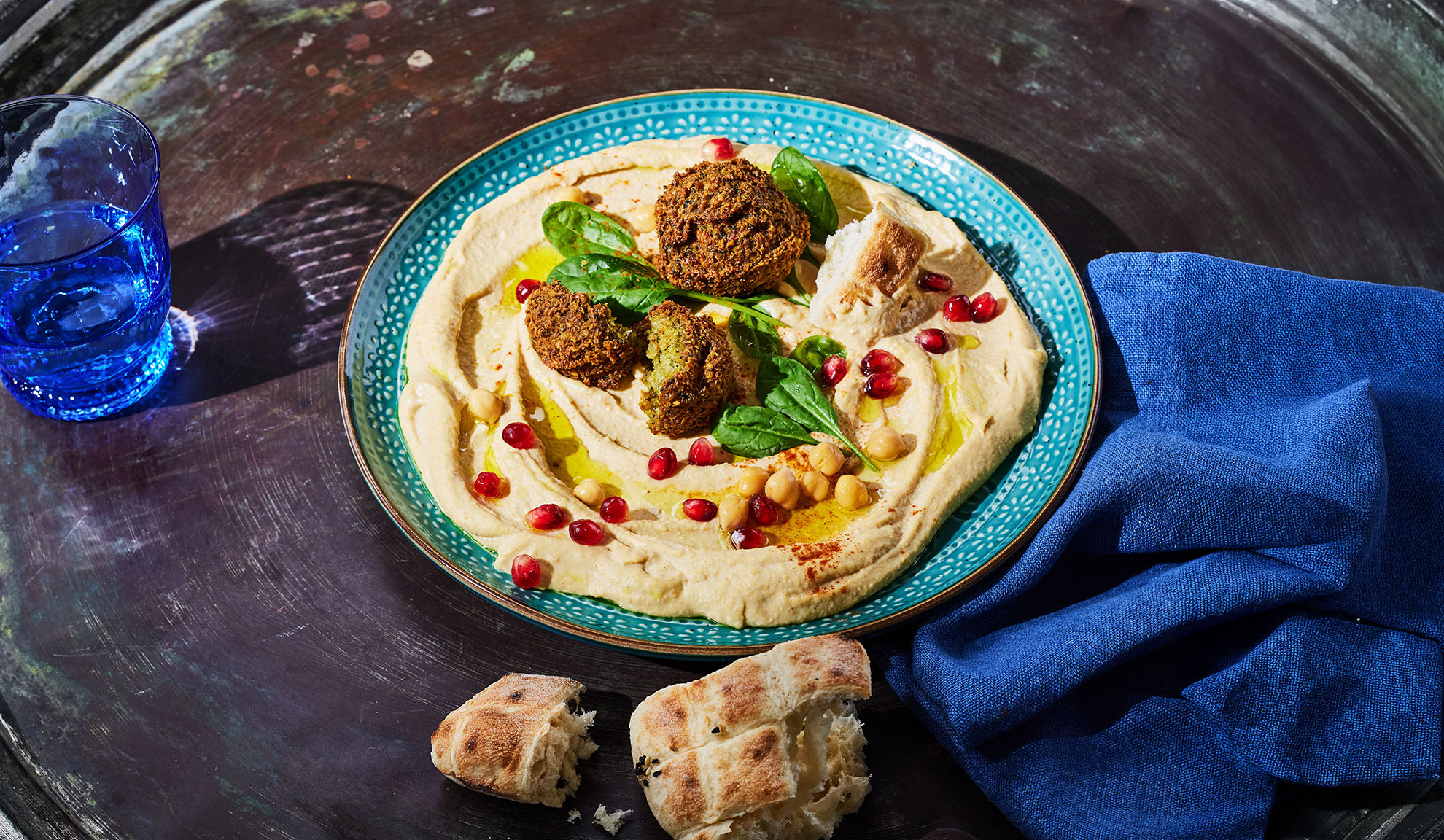 Hummus falafellel, gránátalmamaggal és pitával egy sötét asztalon.