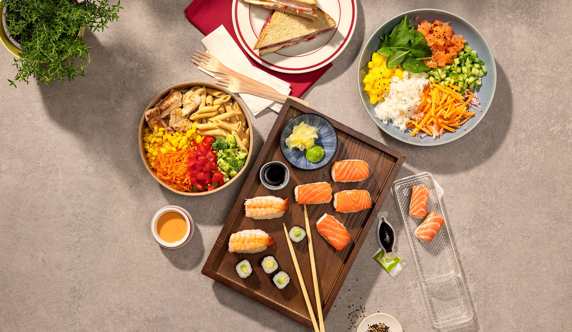 Felülnézeti kép különböző elviteles ételekről: sushi, poke tál, tésztasaláta és szendvicsek.