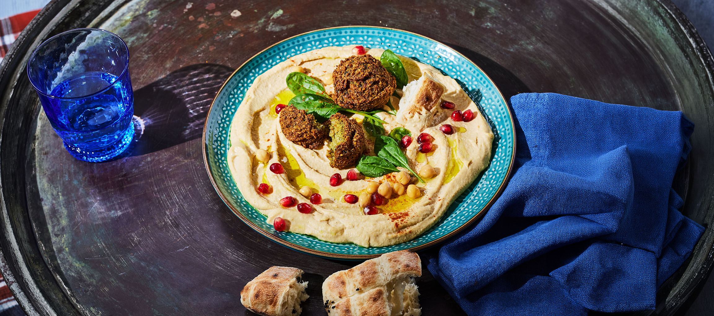 Hummus falafellel, gránátalmamaggal és kenyérrel egy fém tálcán.