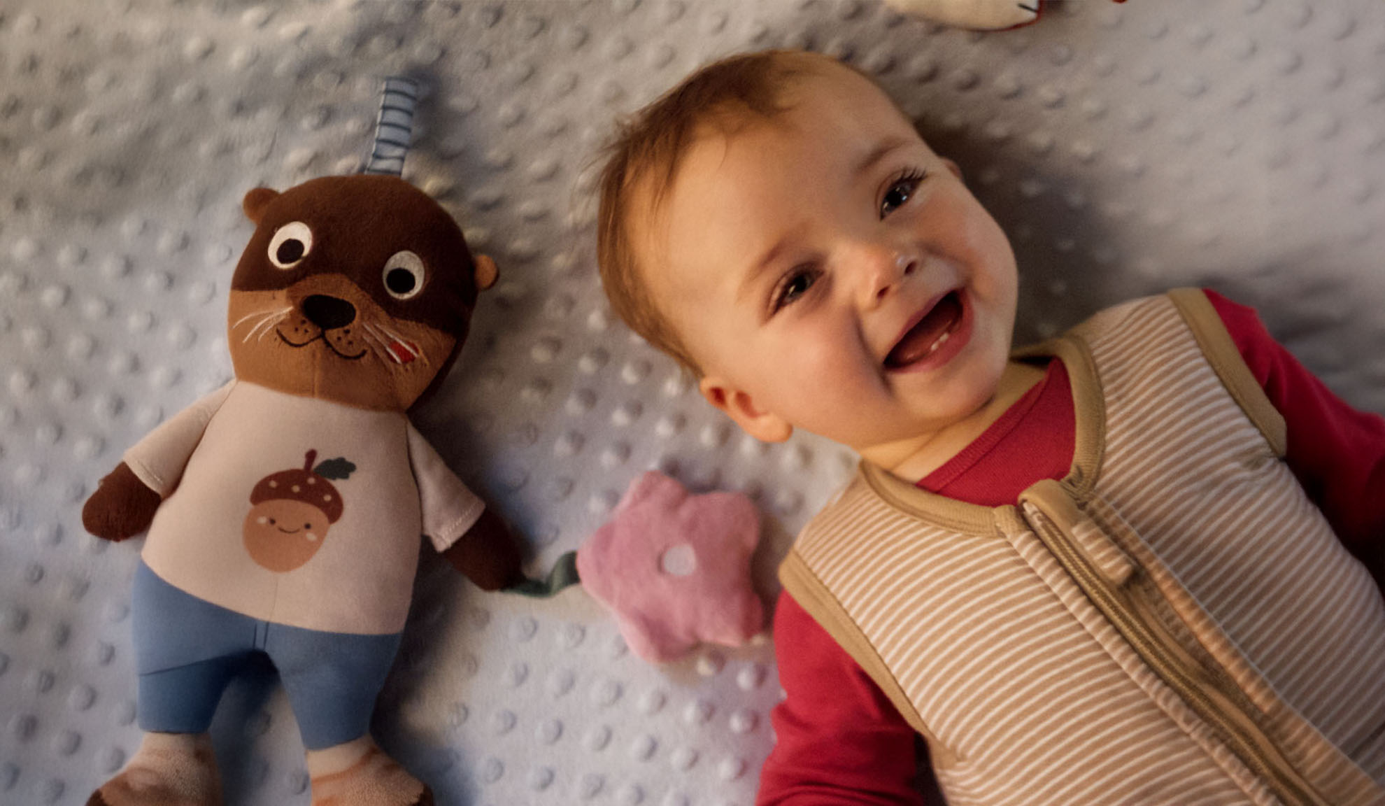 Mosolygó baba és egy vidra plüssjáték egy puha takarón.