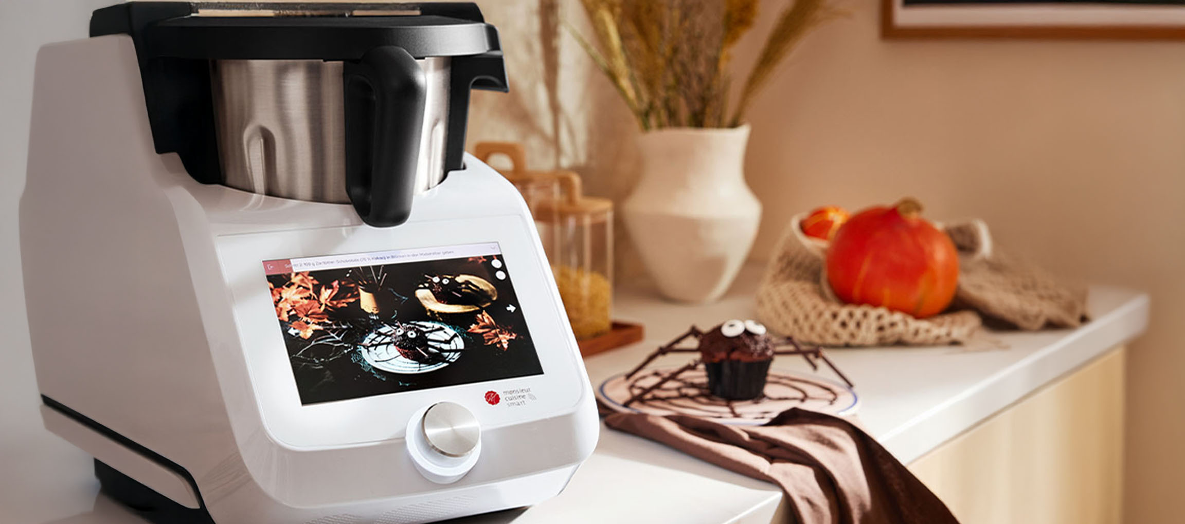 Érintőképernyős konyhai robotgép Halloween receptet mutat, pók-muffin mellett.