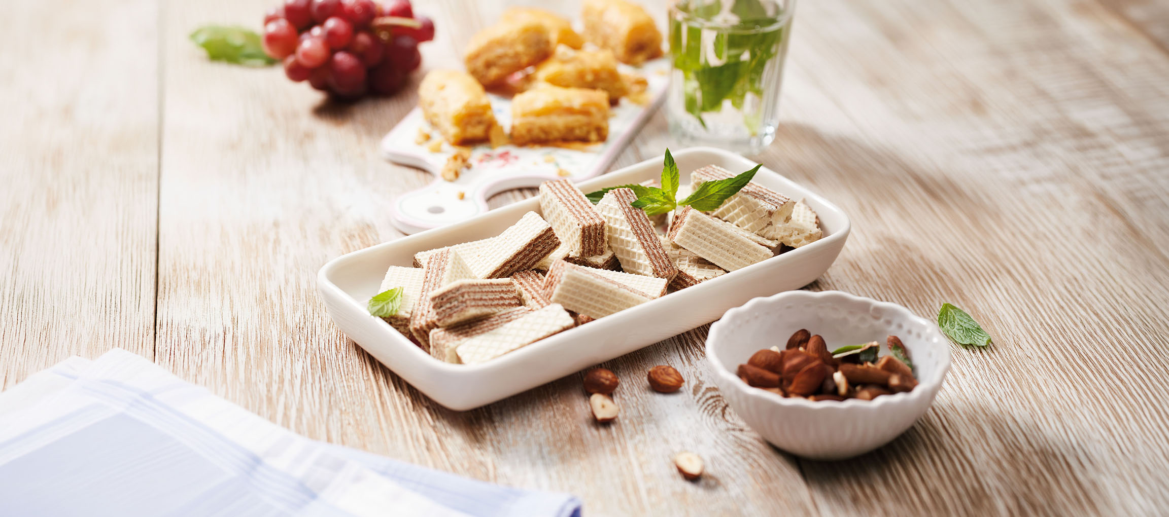 Ostya kekszek, baklava, szőlő és mentás víz egy fa asztalon.