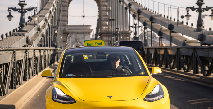 Sárga elektromos autó taxiként egy hídon, sofőrrel a volánnál.