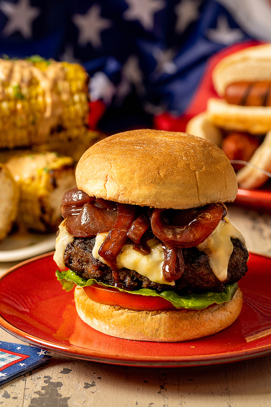 Hamburger karamellizált hagymával és olvasztott sajttal, amerikai zászló előtt.