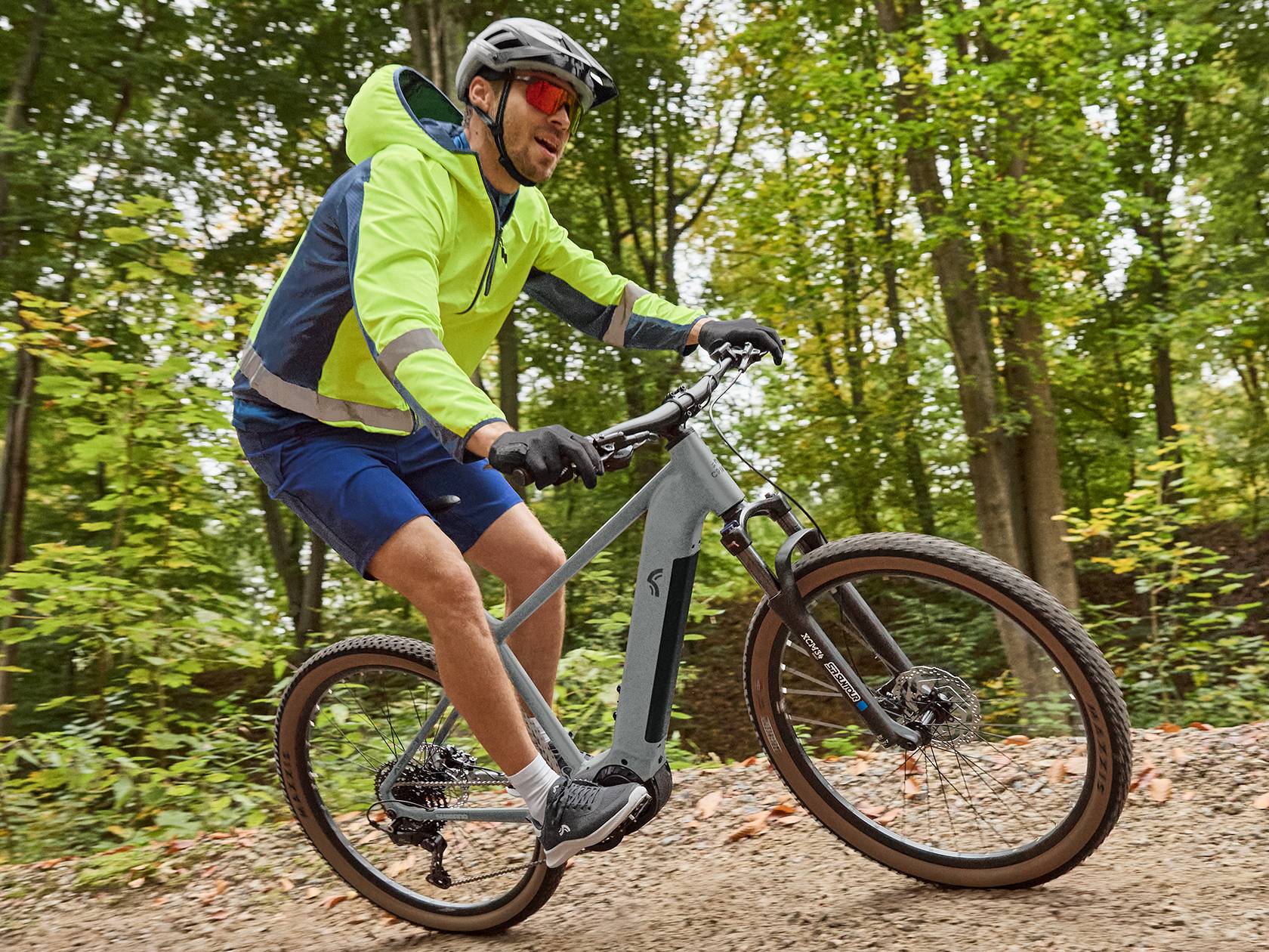 Férfi kerékpáros sisakban és sportruházatban, elektromos kerékpáron, erdei úton.