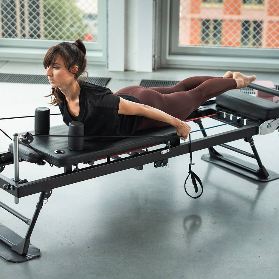 Nő edz Pilates gépen ellenállás szalagokkal.