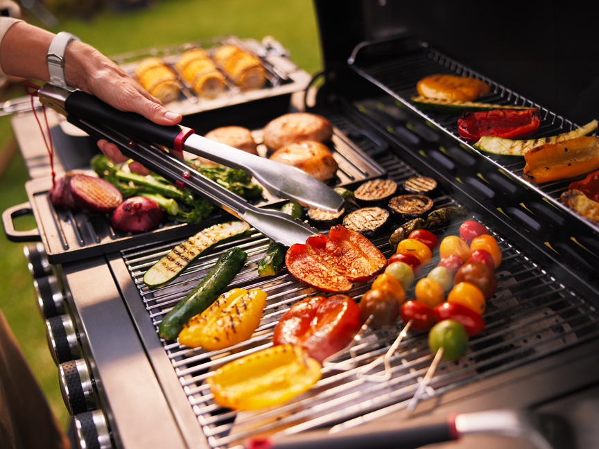 Egy személy grillezett zöldségeket és húst készít egy szabadtéri grillen.