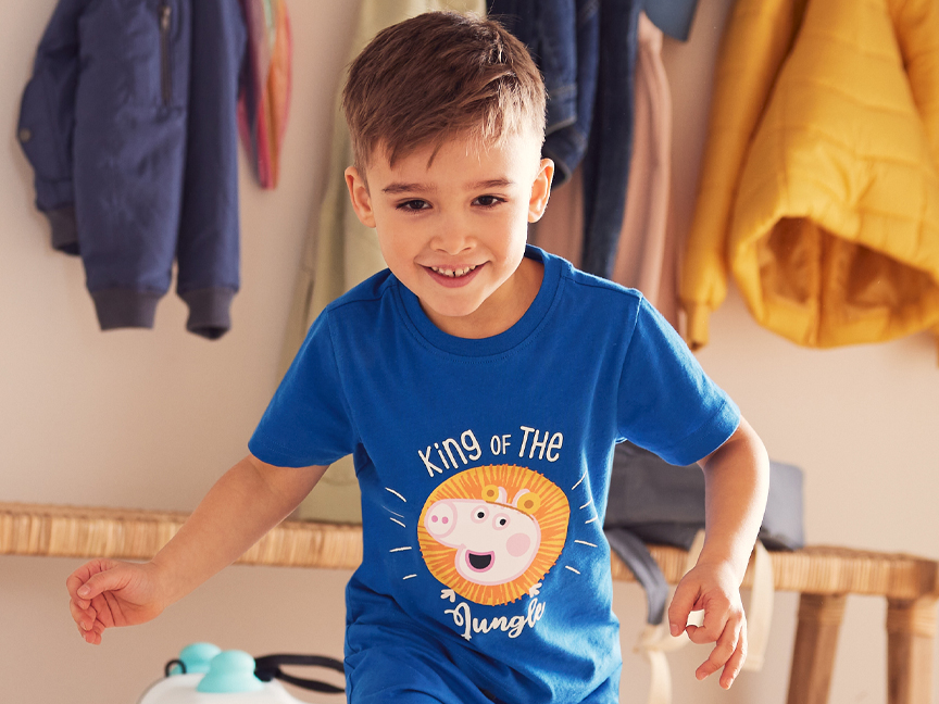 Egy kisfiú Peppa Malac dzsungenkirály pólójában játszik.