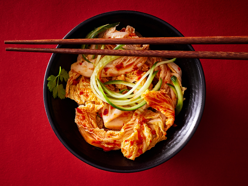 Kimchi tál pálcikákkal, piros háttéren.