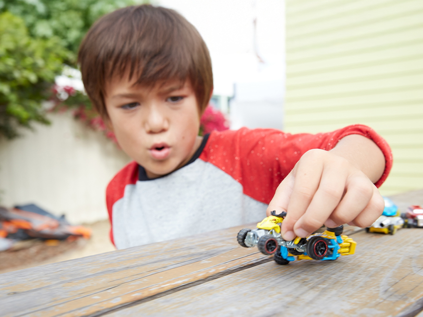 Egy fiú Hot Wheels játékautókkal játszik egy fa asztalon.