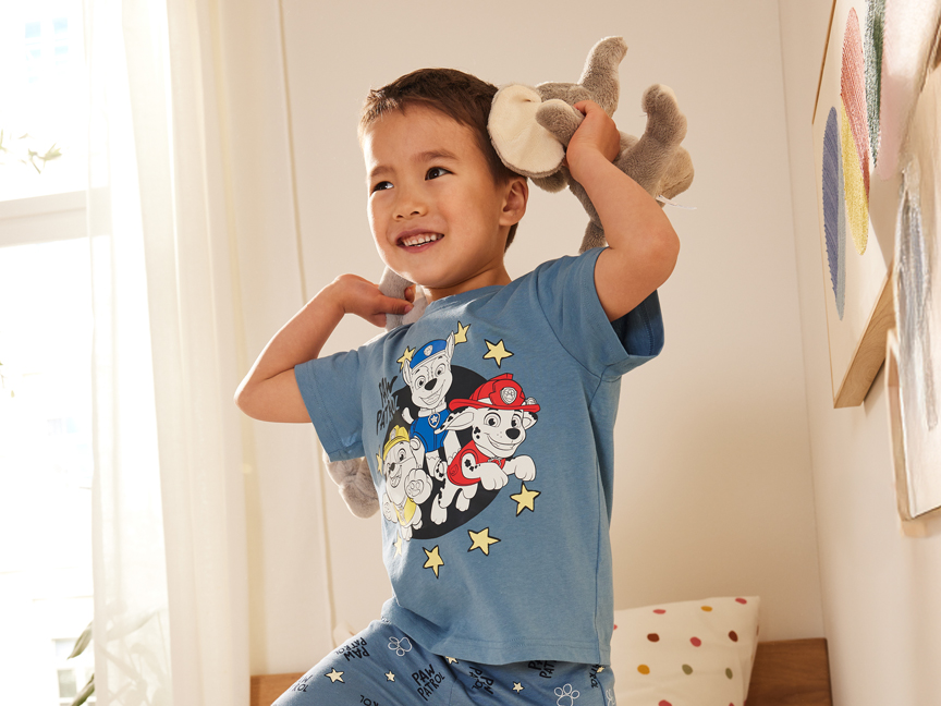 Mosolygós kisfiú Paw Patrol pizsamában, plüssállattal játszik.