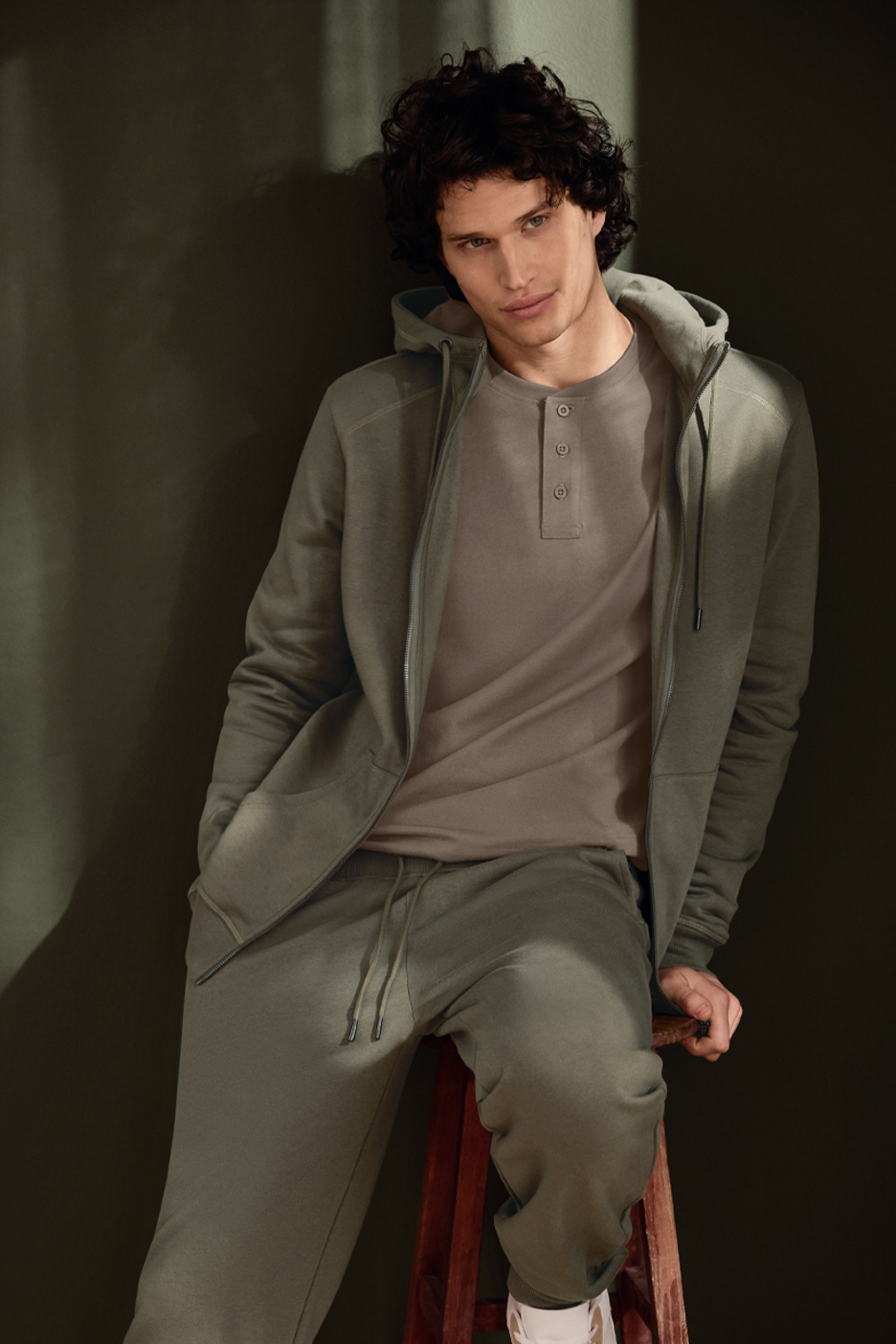 Férfi szabadidőruha szett, zöld cipzáras pulóverrel és nadrággal, bézs pólóval.