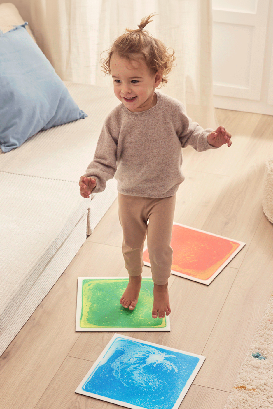 Mosolygós kisgyermek játszik színes folyékony padlólapokon, ugrálva a zöldön.