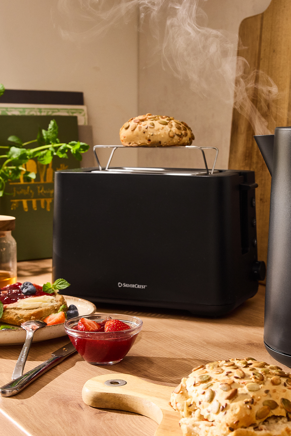Fekete SilverCrest kenyérpirító gőzölgő zsemlével, reggelizőasztalon.