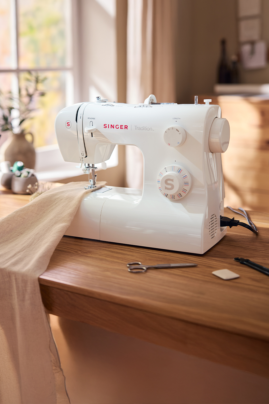 Fehér Singer varrógép világos fa asztalon, anyaggal és varróeszközökkel.
