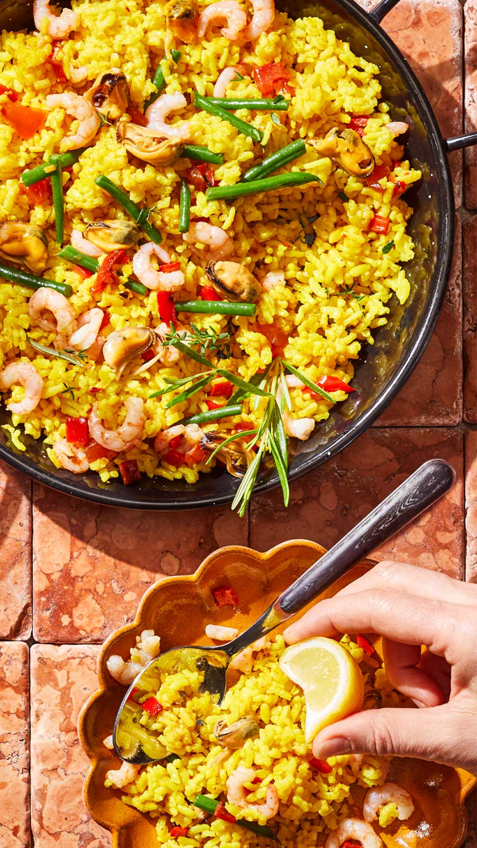 Sárga paella garnélával, kagylóval, zöldbabbal és pirospaprikával, citrommal tálalva.