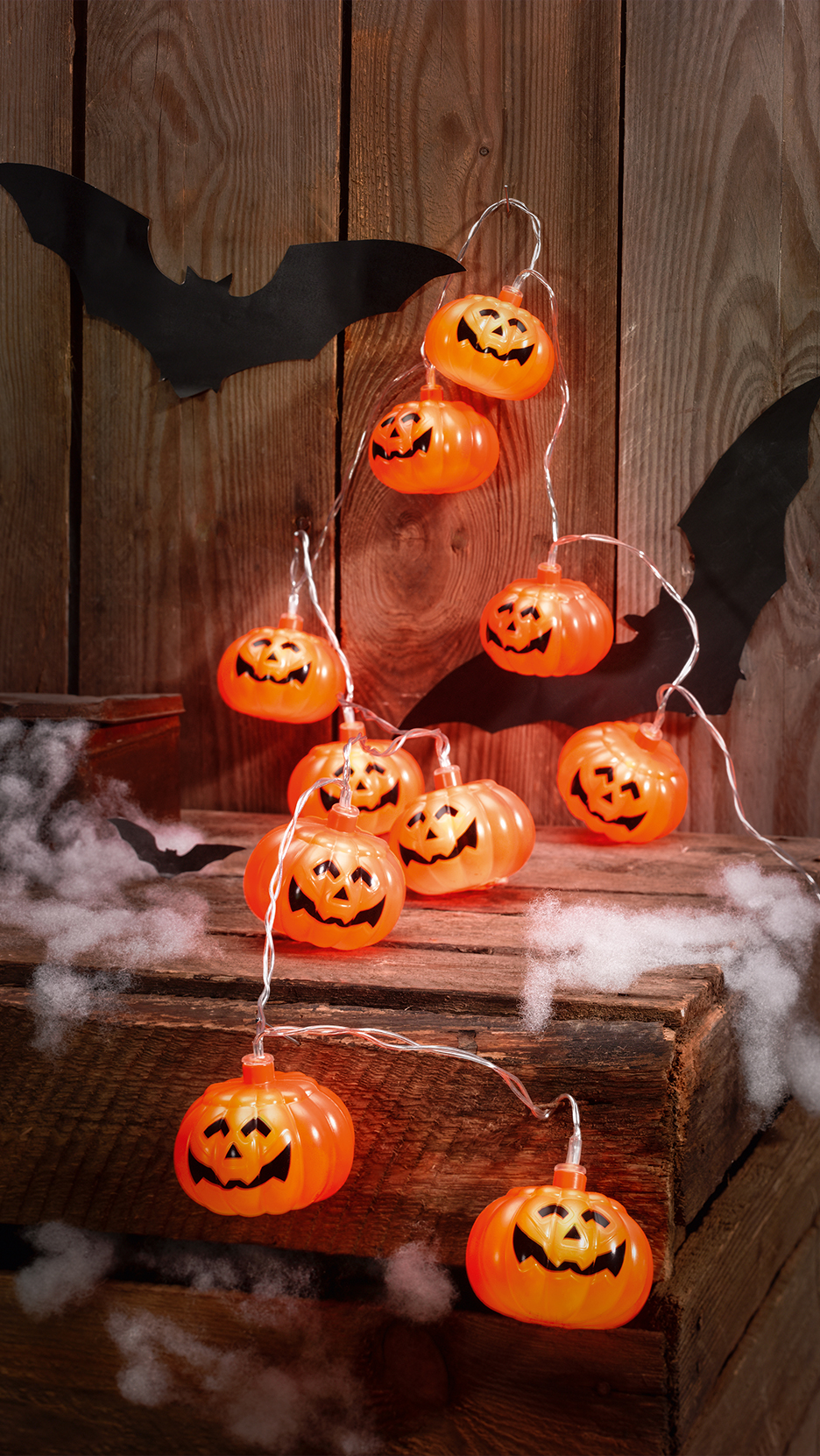 Halloween tök alakú fényfüzér denevérdekorációval és műpókhálóval egy fa háttér előtt.