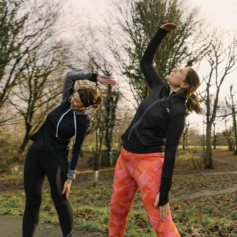 Két nő sportruházatban nyújtózkodik a szabadban.