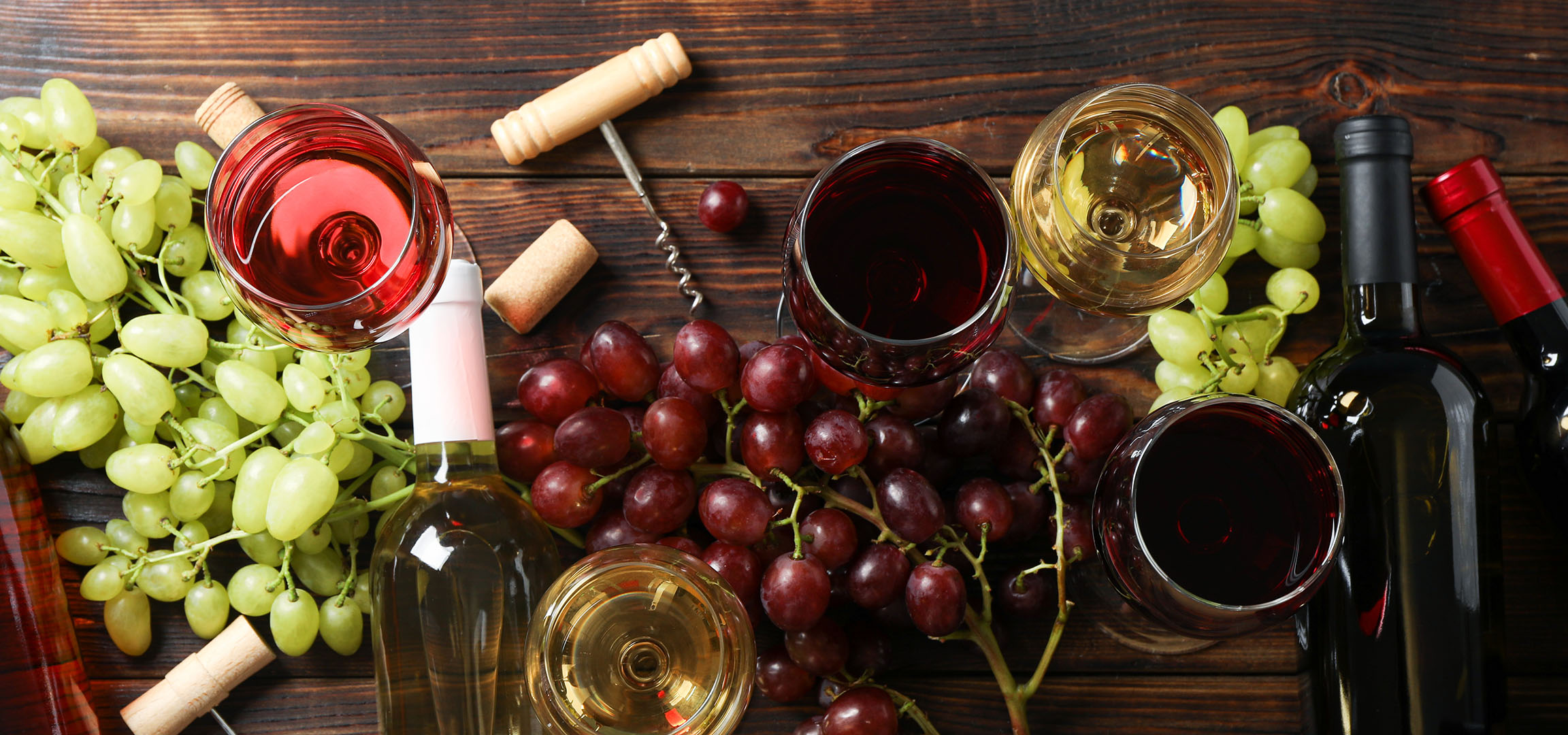 Különböző borok, szőlők és bor kiegészítők egy fa asztalon.