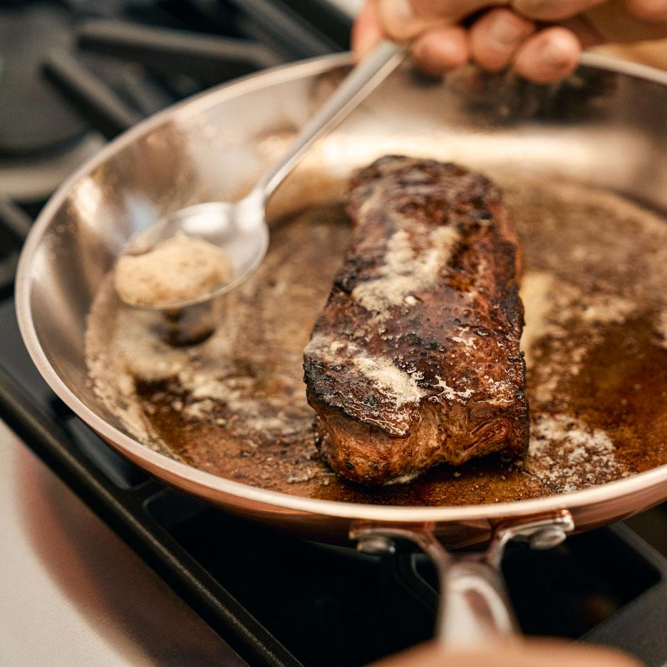 Egy steak sül egy serpenyőben, vajjal locsolva.
