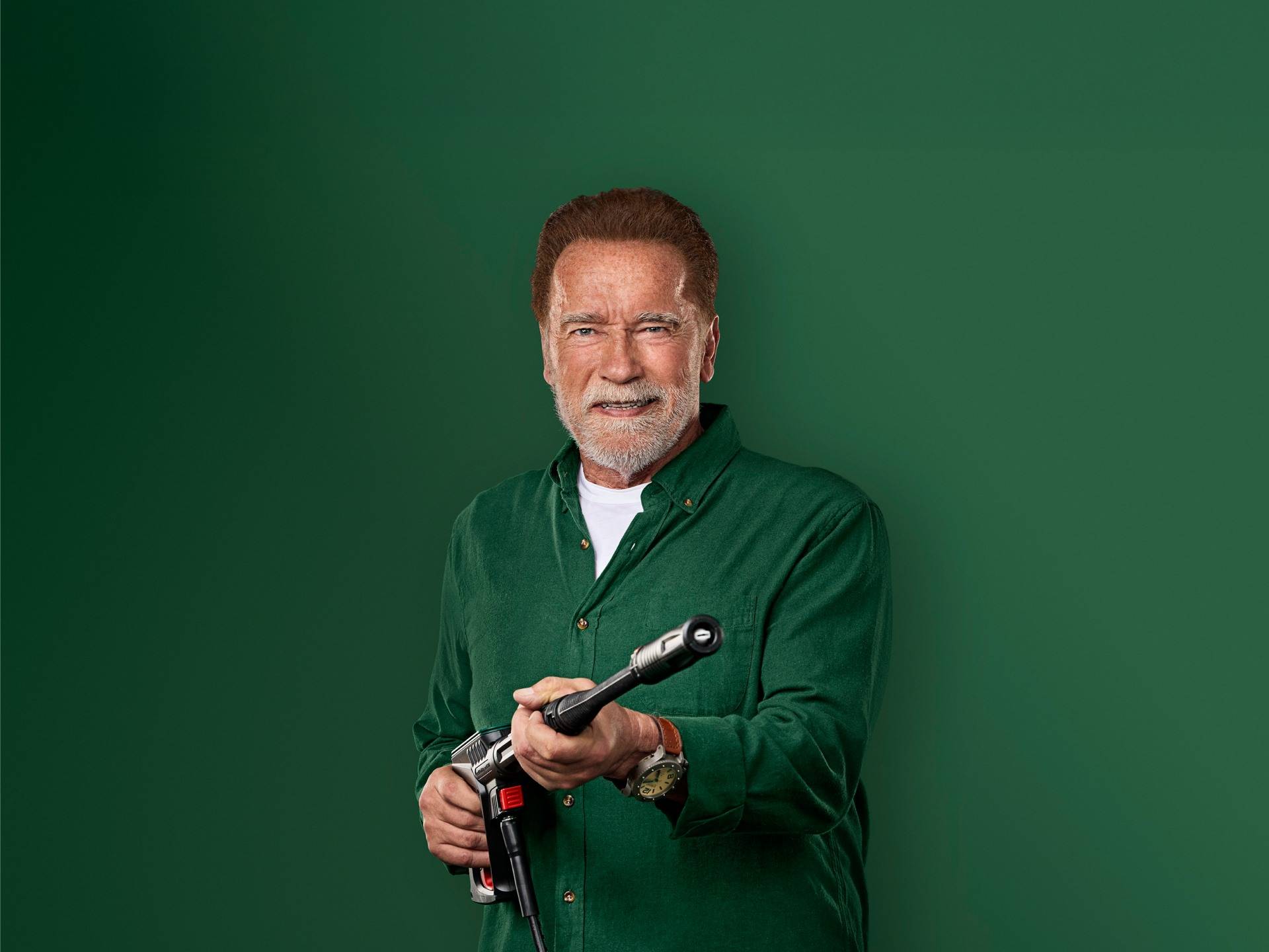 Arnold Schwarzenegger mosolyog, kezében egy nagynyomású mosópisztollyal.
