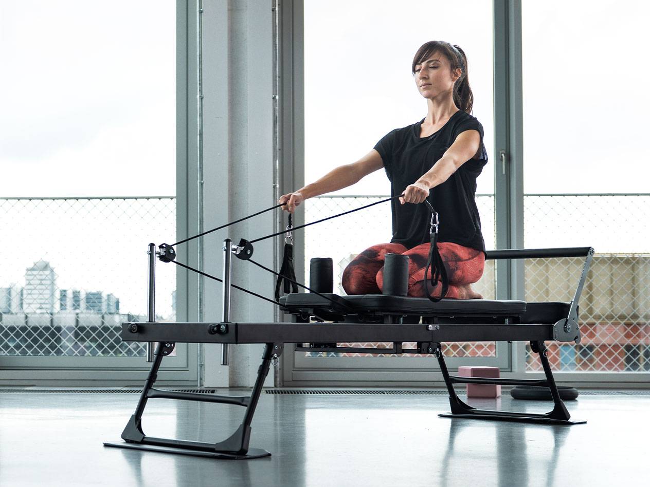 Nő Pilates gyakorlatot végez reformer gépen, városi háttérrel.