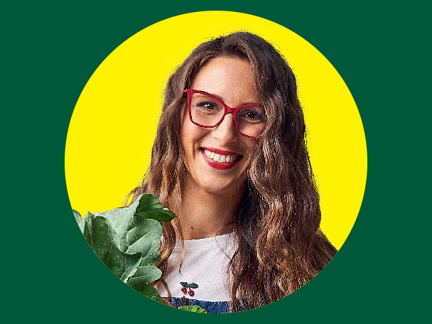 Mosolygó nő piros szemüvegben, kezében zöld leveles zöldséggel.