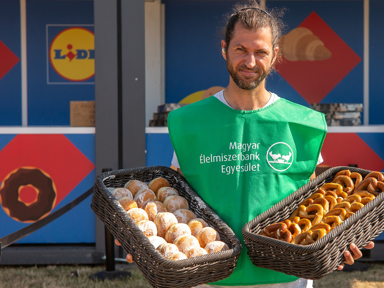 Egy férfi péksüteményekkel teli kosarakat tart a Hungarian Élelmiszerbank Egyesület kötényében.