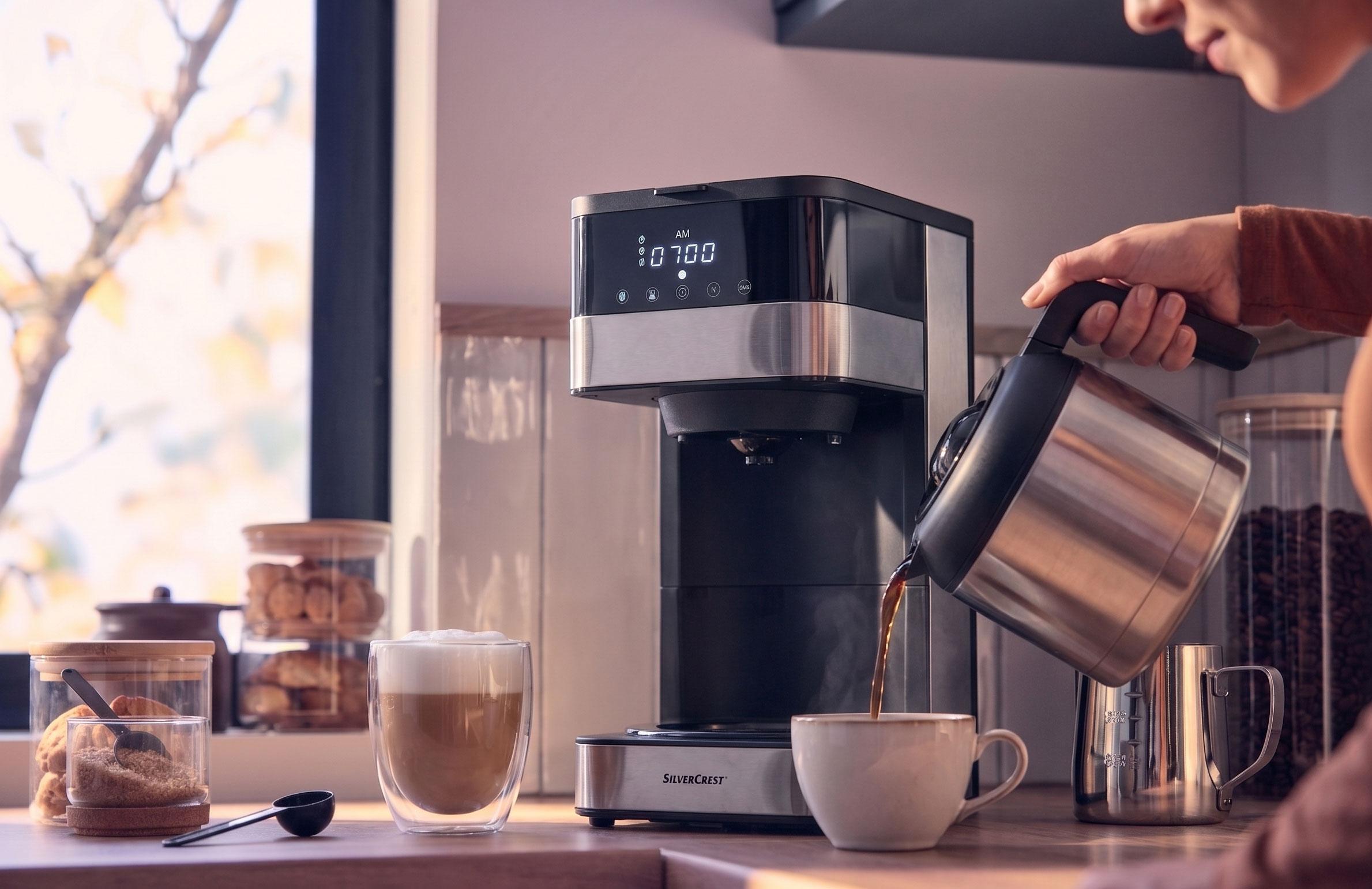 Kávéfőző kávét önt egy csészébe, lattéval és sütikkel a pulton.
