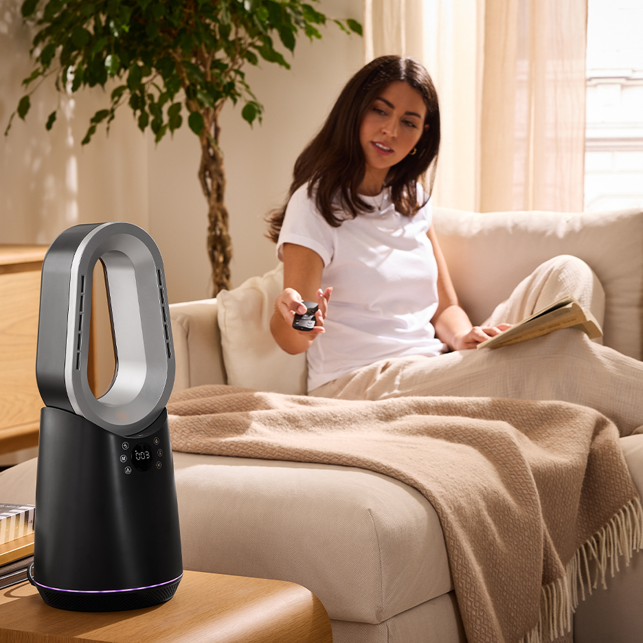 Egy nő a kanapén távirányítóval vezérel egy fekete és ezüst lapát nélküli ventilátort.