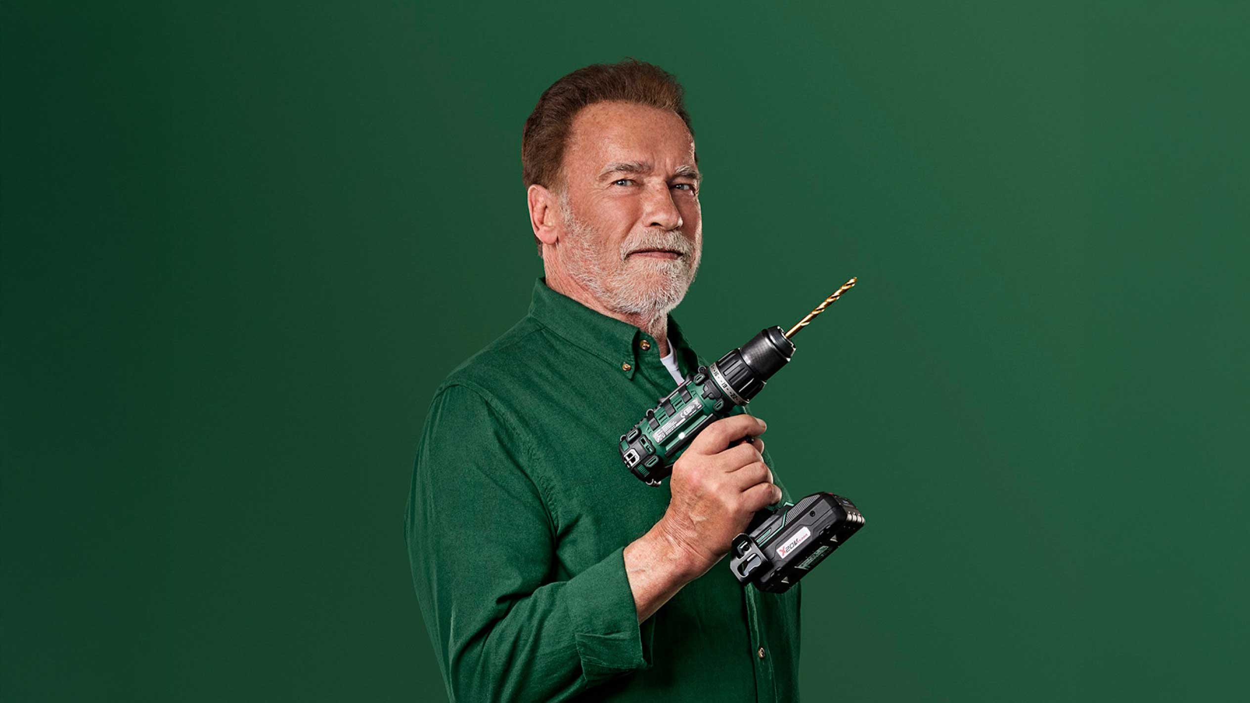 Arnold Schwarzenegger zöld akkus fúrót tart arany fúrófejjel.