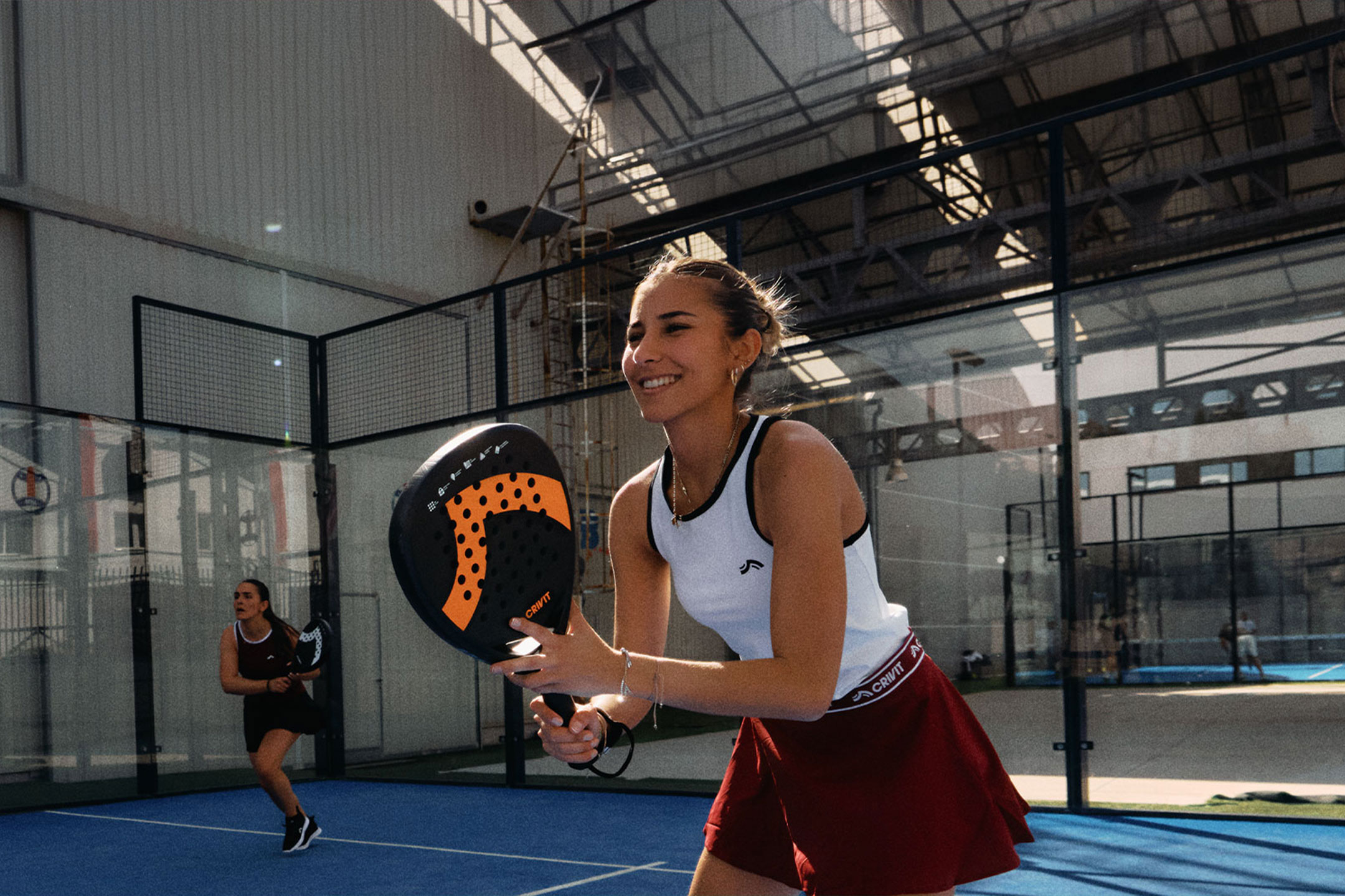 MI/AI segítségével létrehozott/módosított kép: Két nő padel teniszezik, az egyik mosolyog és ütőt tart, kék pályán.