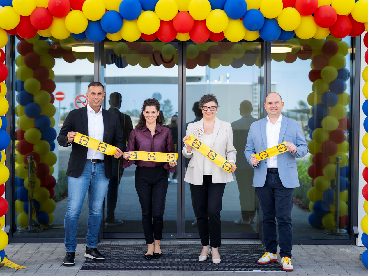Négy mosolygós ember sárga szalagot tart egy új raktár ünnepélyes megnyitóján.