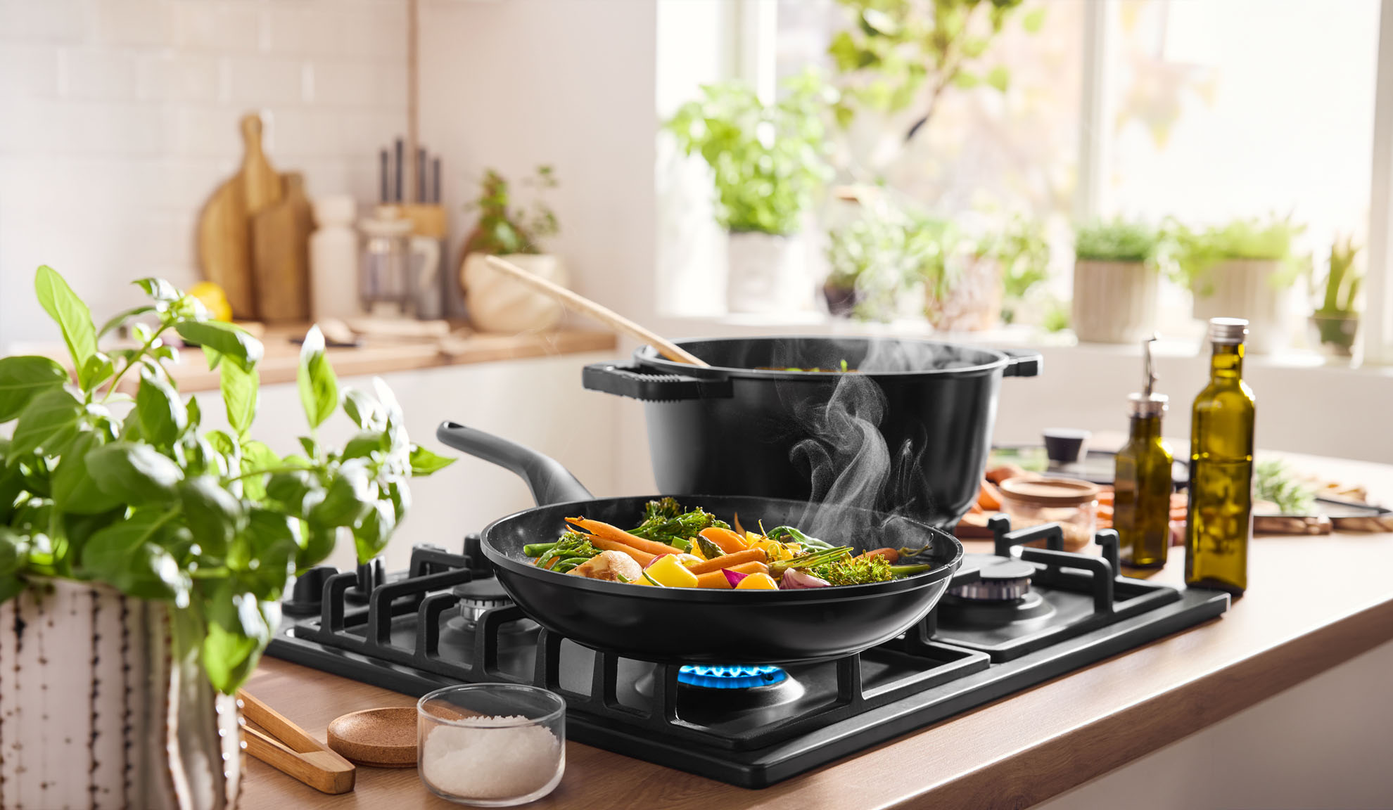 Gőzölgő zöldségek főnek serpenyőben és edényben gázfőzőlapon, világos konyhában.