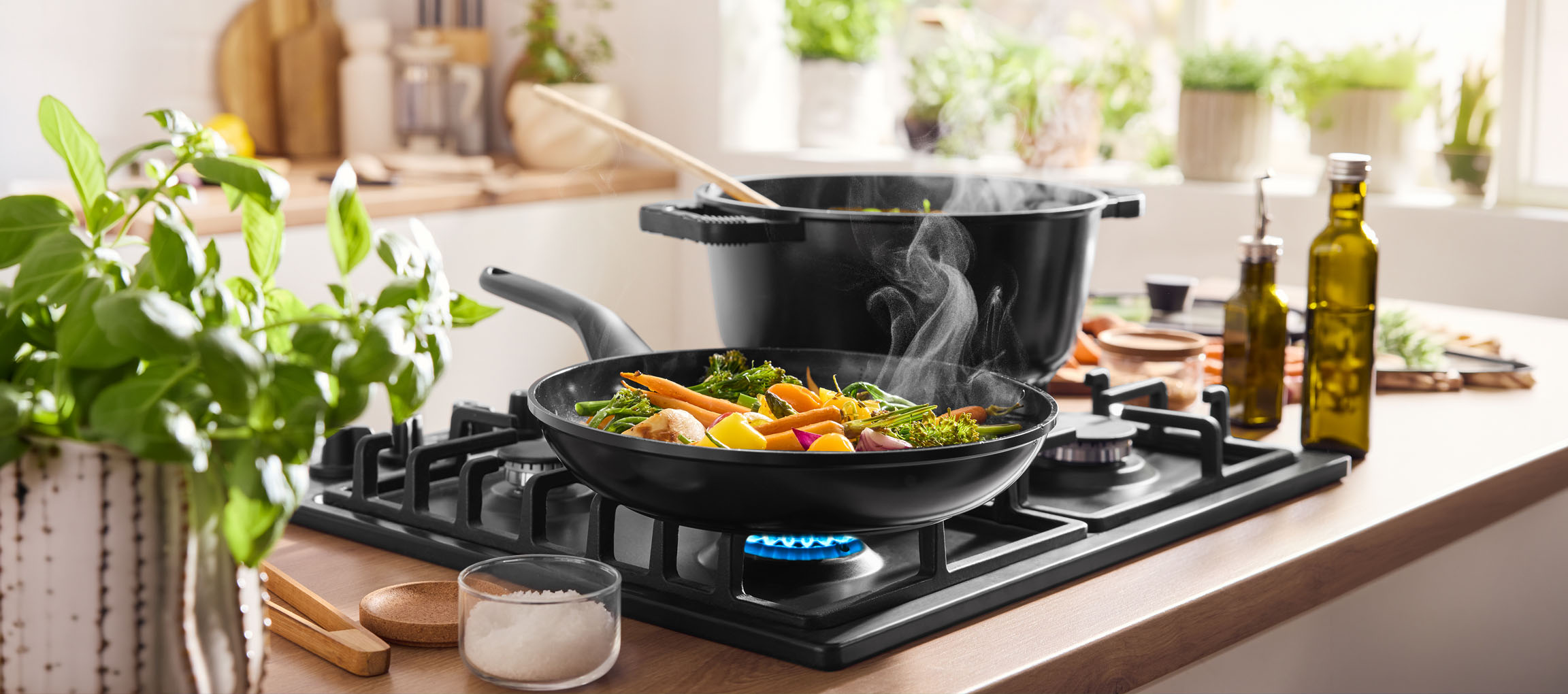 Zöldségek főzése serpenyőben gázfőzőlapon, edénnyel és olívaolajjal a közelben.