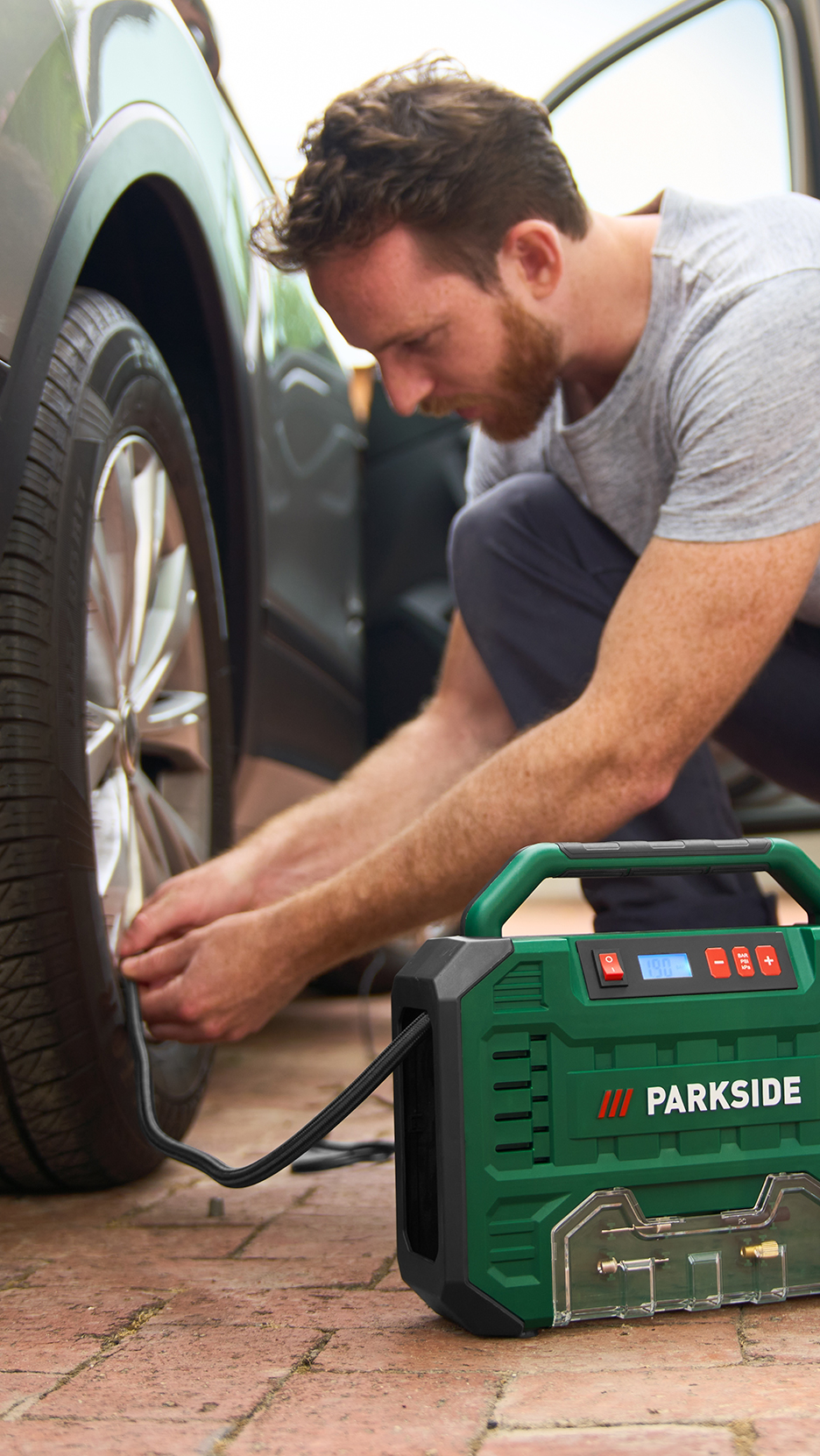 Férfi pumpálja az autó kerekét egy hordozható kompresszorral.