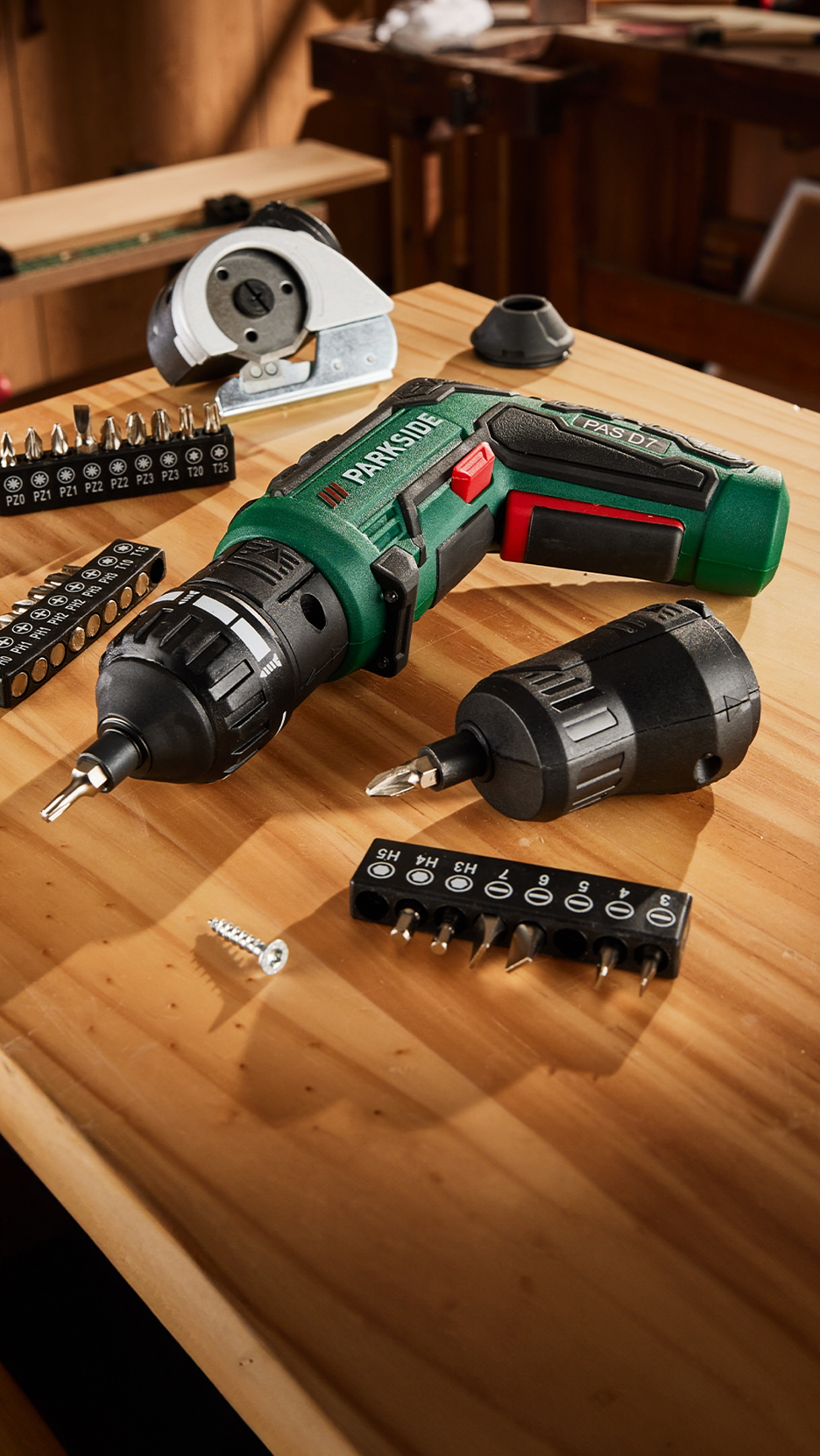 Zöld akkus csavarhúzó, bitkészletekkel és csavarokkal egy fa asztalon.