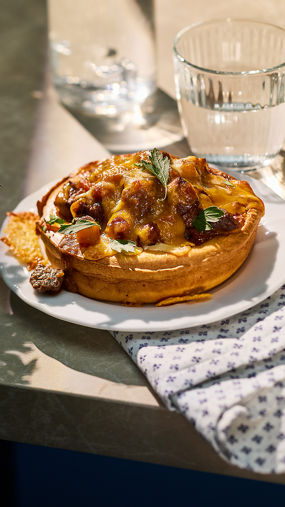 Sült tésztaétel hússal és sajttal, pohár vízzel egy asztalon.