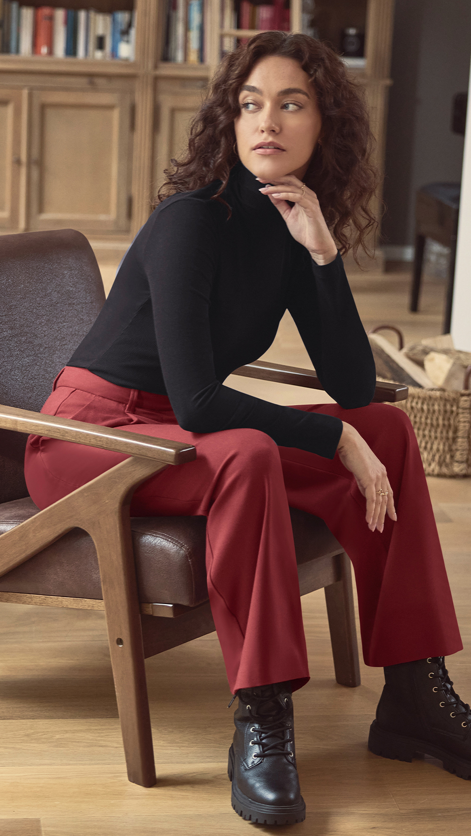 Nő fekete garbóban, piros nadrágban és fekete bakancsban ül egy széken.