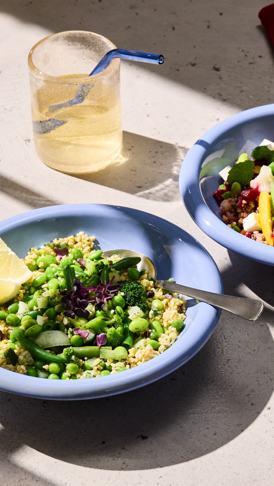 Két tál bulgur saláta zöldségekkel és egy pohár ital egy asztalon.