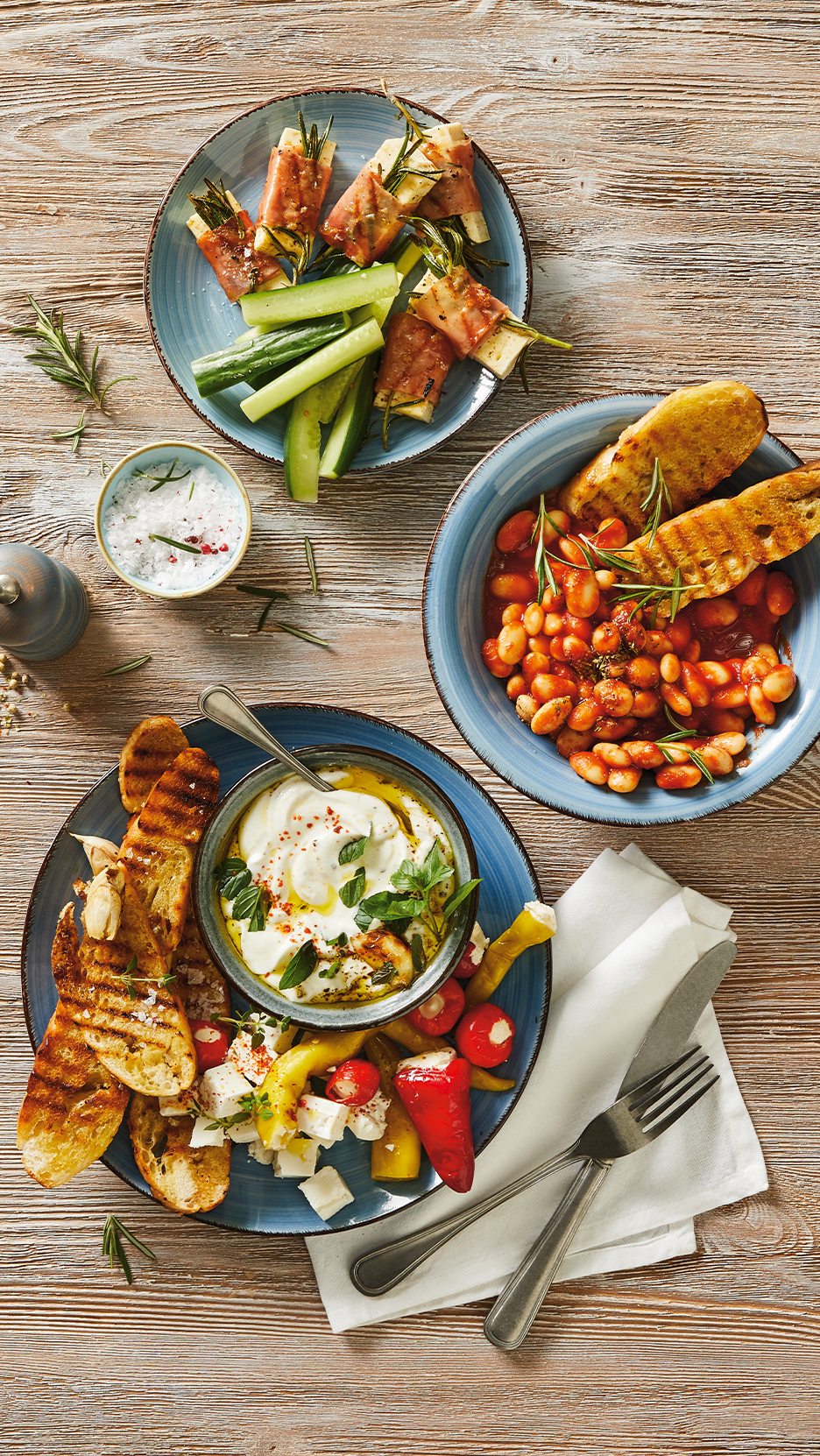 Különféle mediterrán előételek, például sonkába tekert sajt, bab paradicsomszószban, joghurtos mártogatós és grillezett kenyér.