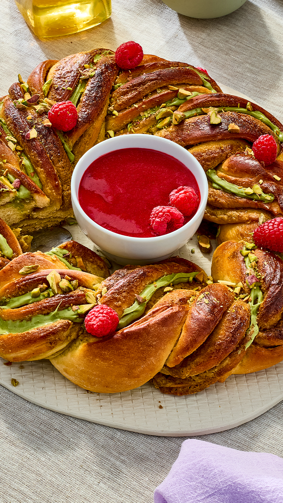 Pistáciás babka málna öntettel és friss málnával díszítve, világos alapon.