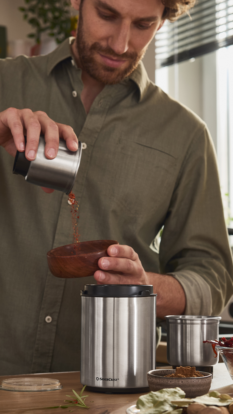 Férfi önt fűszereket egy fa tálba egy rozsdamentes acél kávédaráló mellett.