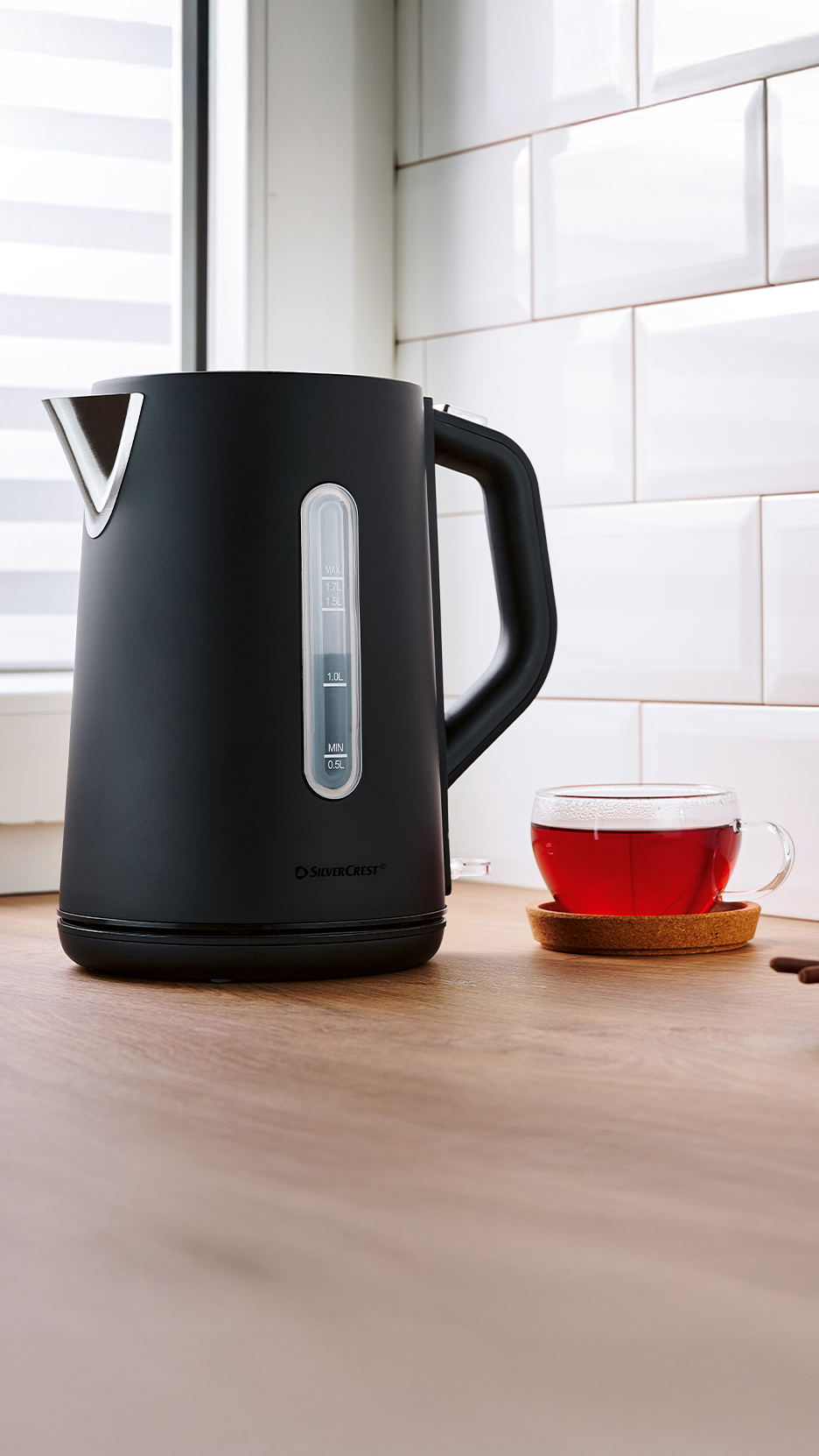 Fekete SilverCrest vízforraló és egy csésze tea egy konyhapulton.
